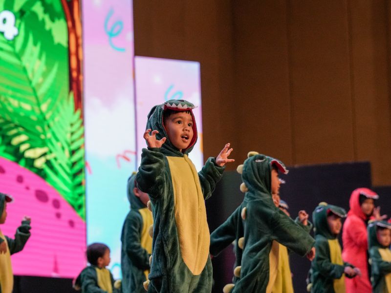 KinderHive child performing in a dinosaur costume during the 2026 Junior Concert