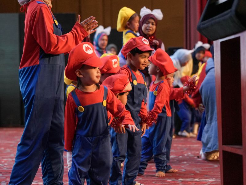 Children performing in colourful Mario-themed costumes at the KinderHive Junior Concert