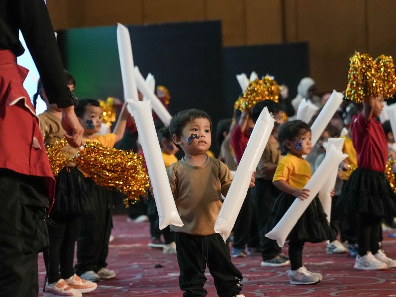 KinderHive children performing with white props and gold pom-poms on stage